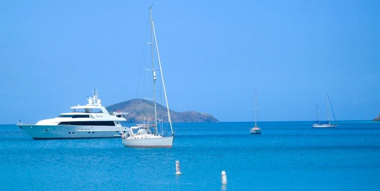 A serene view of yachts anchored in calm blue waters, with an island backdrop.