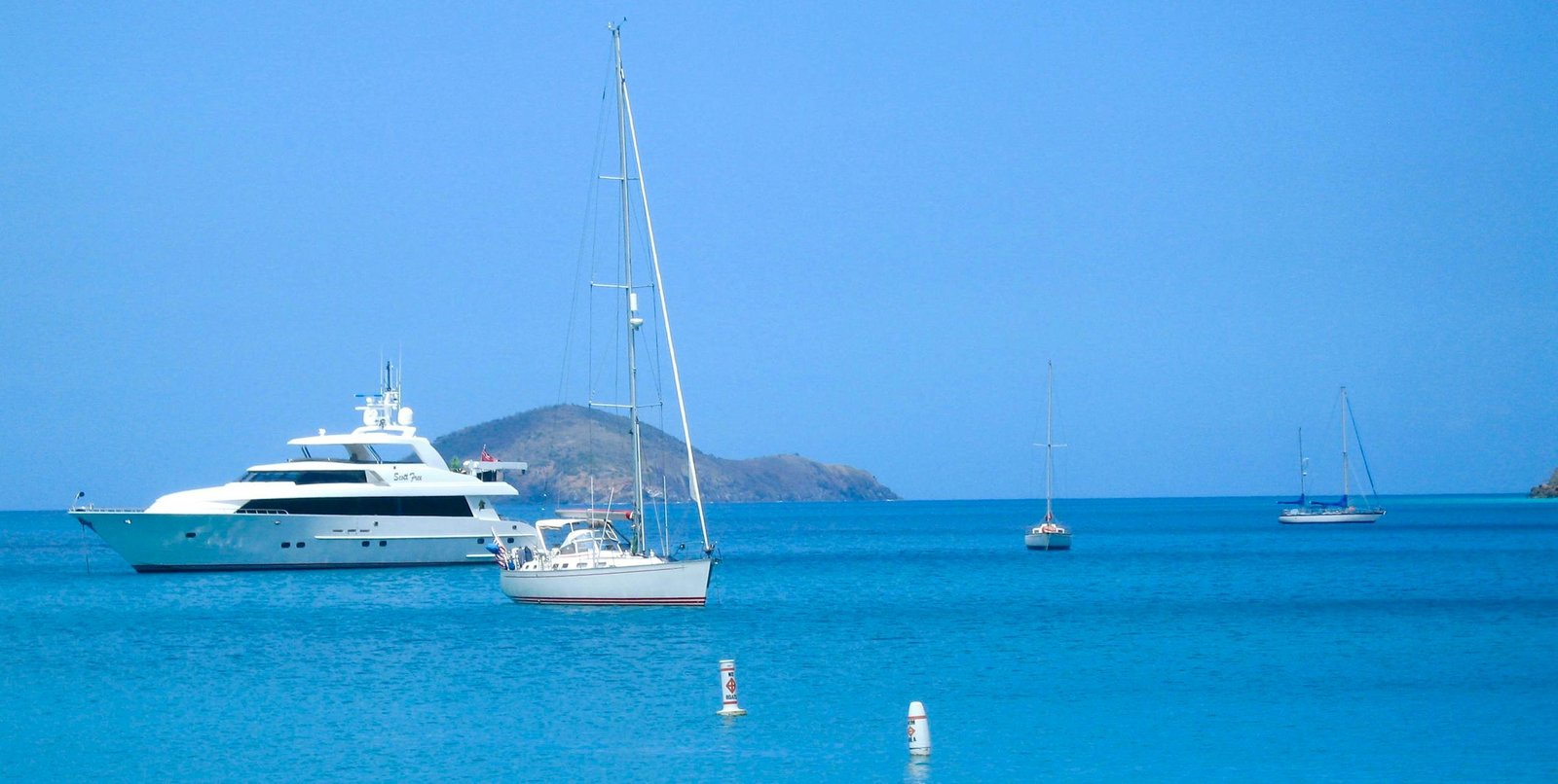 A serene view of yachts anchored in calm blue waters, with an island backdrop.